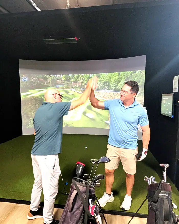 Two golfers high-five in a Pureshot simulator bay after a good shot